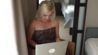 Sırıtan güzel bir kadın, arkadaşlarıyla sohbet ediyor, dizüstü bilgisayar kullanıyor. Mutlu genç bayan promosyon indirimi kodu aldı, internetten alışveriş yaptı, bilet aldı, yemek sipariş etti, kanepede oturdu..