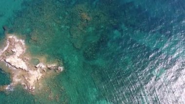 İnsansız hava aracının su altı resiflerindeki görüntüsü ve Akdeniz kıyısındaki şeffaf suyla birlikte plajların yakınındaki kayalıklar. Kamera aşağı bakıyor. Girit, Yunanistan.