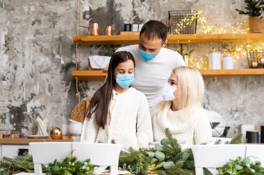 Mutlu bir aile, Noel ağacının yakınındaki COVID-19 koronavirüsünden dolayı tıbbi maske takar. Xmas tatili