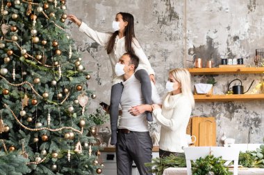 Mutlu bir aile, Noel ağacının yakınındaki COVID-19 koronavirüsünden dolayı tıbbi maske takar. Xmas tatili