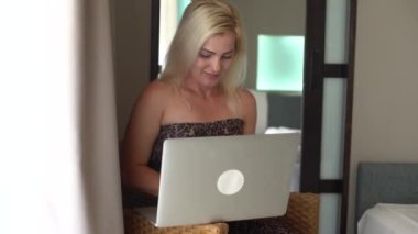 Sırıtan güzel bir kadın, arkadaşlarıyla sohbet ediyor, dizüstü bilgisayar kullanıyor. Mutlu genç bayan promosyon indirimi kodu aldı, internetten alışveriş yaptı, bilet aldı, yemek sipariş etti, kanepede oturdu..