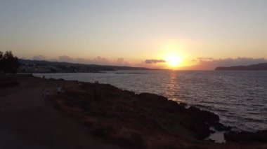 Yunanistan 'ın Girit kentindeki kayalık plajda gün batımının hava manzarası. Gün batımında deniz feneri, sahil boyunca dalgalar....