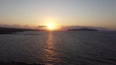 Yunanistan 'ın Girit kentindeki kayalık plajda gün batımının hava manzarası. Gün batımında deniz feneri, sahil boyunca dalgalar....