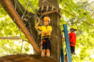 Orman macera parkında bir çocuk. Çocuklar yüksek ip izlerine tırmanıyor. Çeviklik ve çocuklar için açık hava eğlence merkezine tırmanma. Küçük kız dışarıda oynuyor. Okul bahçesinde iple oyun oynanır..