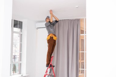 Bir elektrikçi tavana spot ışıkları yerleştiriyor.