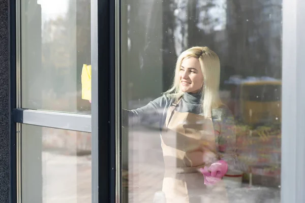Hermosa joven está usando un plumero sonriendo mientras limpia ventanas en la casa —  Fotos de Stock