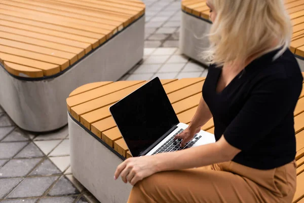 Молодая женщина носит умные часы, используя ноутбук. Женщина работает на ноутбуке в кафе под открытым небом . — стоковое фото