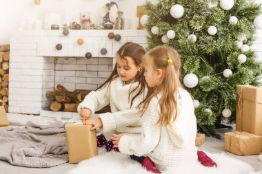 Noel ağacının önünde iki kız hediye ve şömineyle