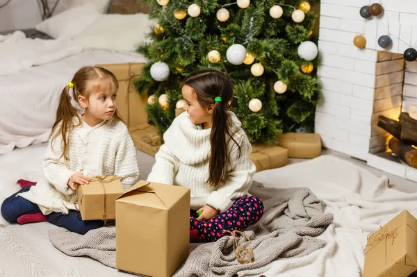 Δύο κορίτσια μπροστά από το χριστουγεννιάτικο δέντρο με δώρα και τζάκι — Φωτογραφία Αρχείου