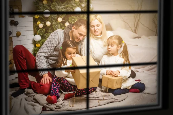 Famiglia che scambia regali davanti all'albero di Natale attraverso la finestra — Foto Stock