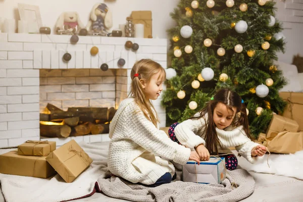 Twee meisjes in de voorkant van kerstboom met geschenken en open haard — Stockfoto