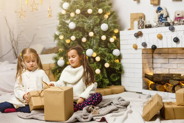 Dwie dziewczyny przed choinką z prezentami i kominkiem — Zdjęcie stockowe