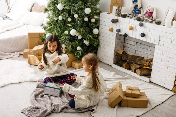 Twee meisjes in de voorkant van kerstboom met geschenken en open haard — Stockfoto