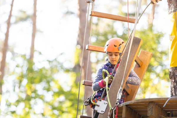 어린 소녀가 로프 위에서 서 손으로 밧줄을 잡고 있습니다. 밧줄 공원에 있는 어린이는 장애물을 지나간다 — 스톡 사진