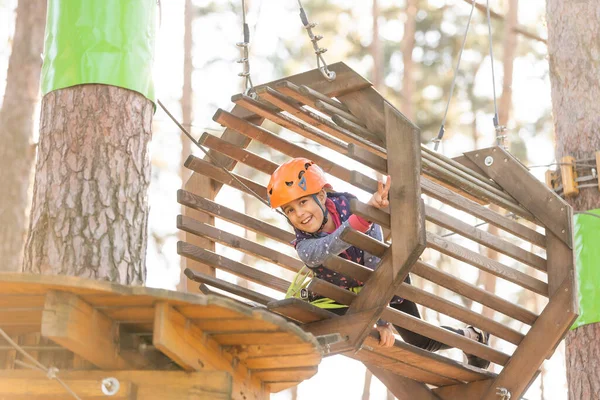 La chica en el casco naranja en la aventura Parque se aferra a las cuerdas — Foto de Stock