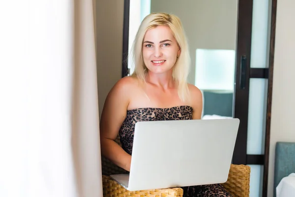 Ευτυχισμένη περιστασιακή όμορφη γυναίκα που εργάζεται σε ένα φορητό υπολογιστή κάθεται στο κρεβάτι στο σπίτι. — Φωτογραφία Αρχείου