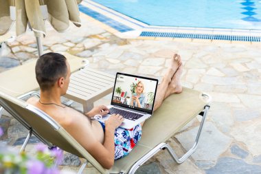 çekici bir genç adam tropikal otel bahçesinde bırakmasını iken bir dizüstü bilgisayar kullanarak.