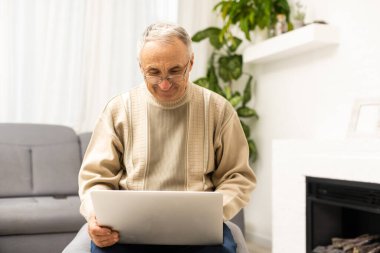 Evde dizüstü bilgisayar kullanan gözlüklü yaşlı adam.