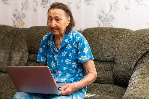 Donna molto vecchia utilizzando computer portatile seduto nel suo divano — Foto Stock