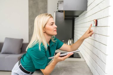 Akıllı ev dijital termostatı dokunmatik ekranlı kadın oturma odasının duvarındaki ısıyı ayarlamak için dokunmatik ekrana dokunuyor