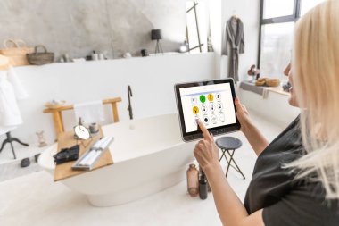 Kadın elleri ekranda akıllı ev sistemi olan bir tablet bilgisayarı tutuyor