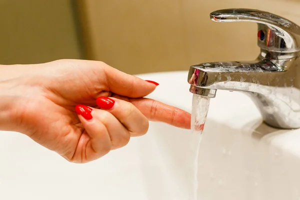 Nahaufnahme an den Fingern in der Nähe des Wasserhahns von Waschbecken oder Badewanne im heimischen Badezimmer. Hündin zu Hause überprüft fließendes Wasser mit der Hand — Stockfoto