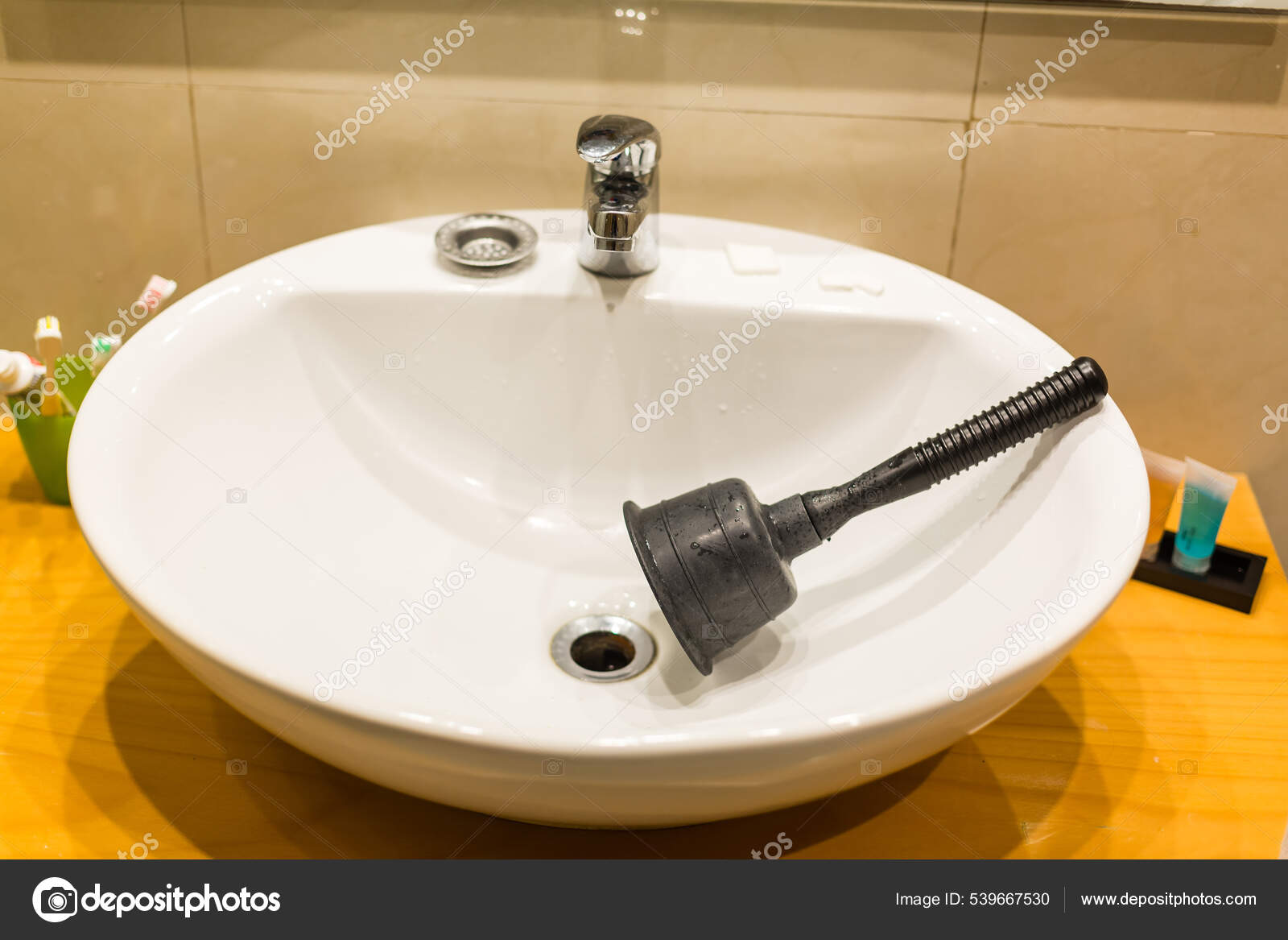 Household black sink plunger tool in bathroom sink plugged with pink  material dishrag, flattened draining tool with rubber cup and wooden shaft  or stick, water pouring from the tap. Horizontal Stock Photo