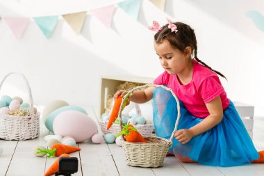 Paskalya 'ya hazırlanıyorum. Paskalya yumurtası tutan ve arka planda süslemelerle gülümseyen sevimli küçük kız.
