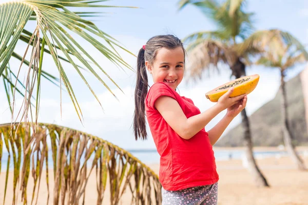 Портрет милой маленькой девочки с папайей на фоне пальм — стоковое фото