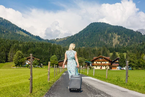 Yazın bir kadın tatile çıkıyor, doğa ve dağların arka planında bir bavulla tatile. Seyahat konsepti, dağlarda güzel bir yerde hafta sonu. — Stok fotoğraf