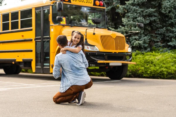 Девочка с отцом возвращаются в школу возле школьного автобуса — стоковое фото