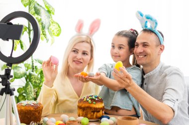 Aile, Paskalya tatilinde arkadaşlarıyla özel bir program kullanarak internet üzerinden iletişim kurar. İş arkadaşlarına tablet üzerinden video konferansı. Çiçekler ve renkli yumurtalarla süslenmiş bir masa.