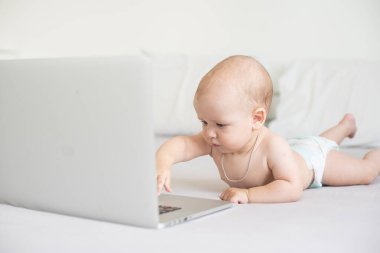 Beyaz yatakta dizüstü bilgisayarı olan şirin bir bebek.