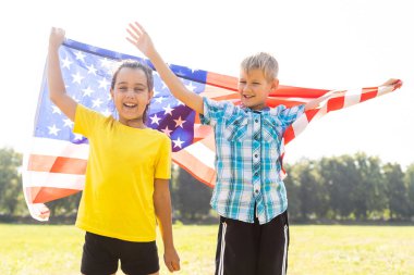 4 Temmuz, Bağımsızlık Günü, Bayrak Günü konseptini kutlamak için el ele tutuşup Amerikan bayrağı sallayan mutlu beyaz kız ve oğlan gülümsüyor..