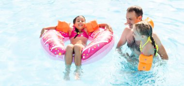 Denizde tropik bir tatil köyünde mavi yüzme havuzunda oynayan mutlu bir aile. Yaz tatilleri konsepti.