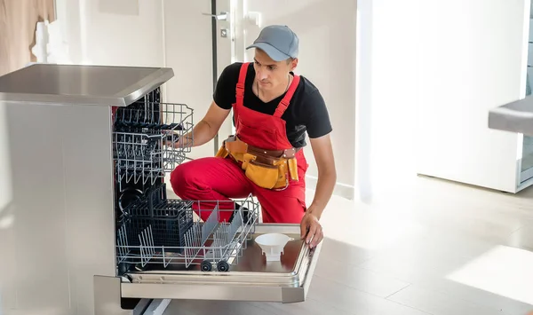 Мастер устанавливает посудомоечную машину в кухонный шкаф — стоковое фото