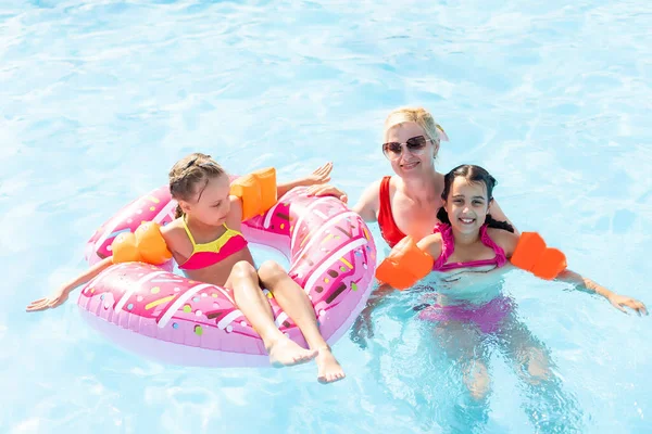 Familia feliz en la piscina, divirtiéndose en el agua, madre con niños disfrutando del parque acuático, resort de playa, vacaciones de verano, concepto de vacaciones — Foto de Stock