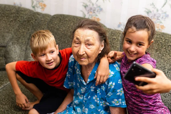 Overgrootmoeder met kinderen. Familie. Een schooljongen en een peutermeisje. Gelukkige oudere oude vrouw en kleinkinderen, binnen. — Stockfoto