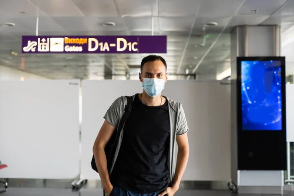 Jeune Européen en manteau gris, masque médical jetable protecteur à l'aéroport. Peur du dangereux coronavirus grippal N-CoV 2019. sac à dos, valise. — Photo