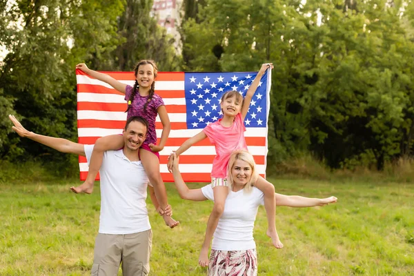 Patriotic holiday. Happy family, mother and daughters with American flag outdoors on sunset. USA celebrate independence day 4th of July. — Stock Photo, Image