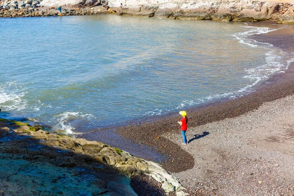 Menina senta-se em uma costa rochosa e olha para o mar — Fotografia de Stock