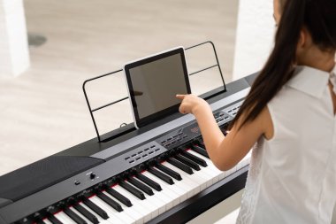 Küçük kız evde tabletle sınıf eğitiminde piyano çalıyor. İnternette covid-19 kriz karantinasında öğreniyor.