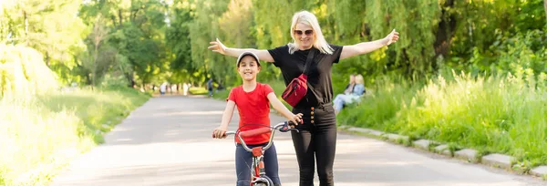 Vacker ung mor lär sin dotter att cykla. Både leende, sommarpark i bakgrunden, aktivt familjekoncept — Stockfoto