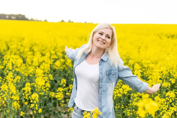 Retrato de mulher atraente no campo de colza florescente com luz do pôr do sol. Flores amarelas e mulher feliz — Fotografia de Stock