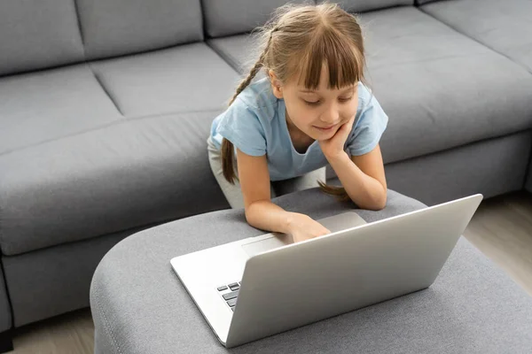 Nudná holčička s laptopem doma. Roztomilé dítě dělá domácí úkoly na počítači. Moderní online vzdělávací, komunikační a technologický koncept, kopírovací prostor. — Stock fotografie