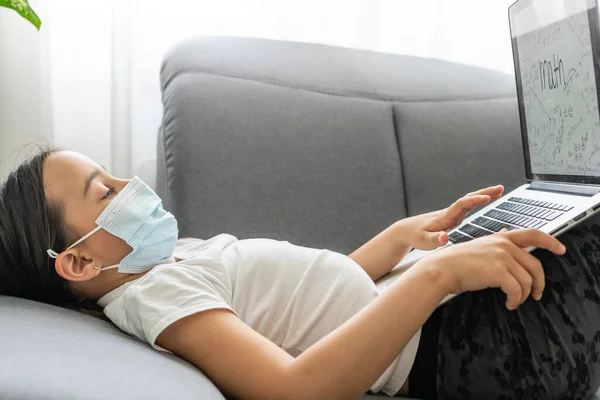 Το έξυπνο κοριτσάκι που φοράει μάσκα κάνει ασκήσεις στο σαλόνι της. Shes Sitting and Uses Laptop. — Φωτογραφία Αρχείου