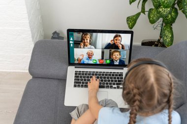Genç bir kızın evde oturup konuşmasına, öğretmeniyle veya öğretmeniyle çevrimiçi video dersi almasına webcam sohbetine katılan genç bir kız çocuğuna, dizüstü bilgisayarında uzak kullanım konferansı uygulamasına çalışmasına.