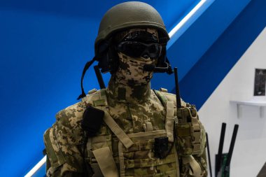 Askeri üniformalı ve teçhizatlı manken. Güvenlik kaskı ve gözlükleri. Özel telsiz iletişim cihazı. Modern savaş tesisleri.