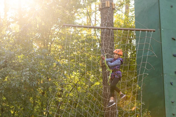 Kind in bos avonturenpark. Kinderen klimmen op het hoge touwspoor. Agility en klimmen buiten amusement centrum voor kinderen. Klein meisje dat buiten speelt. Schoolplein speeltuin met touw weg. — Stockfoto