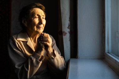 Dua eden yaşlı bir kadının yakın portresi.